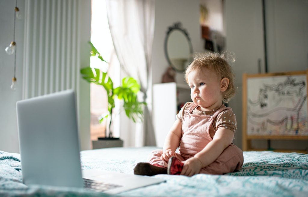 Small toddler girl on bed at home, watching story tales on laptop